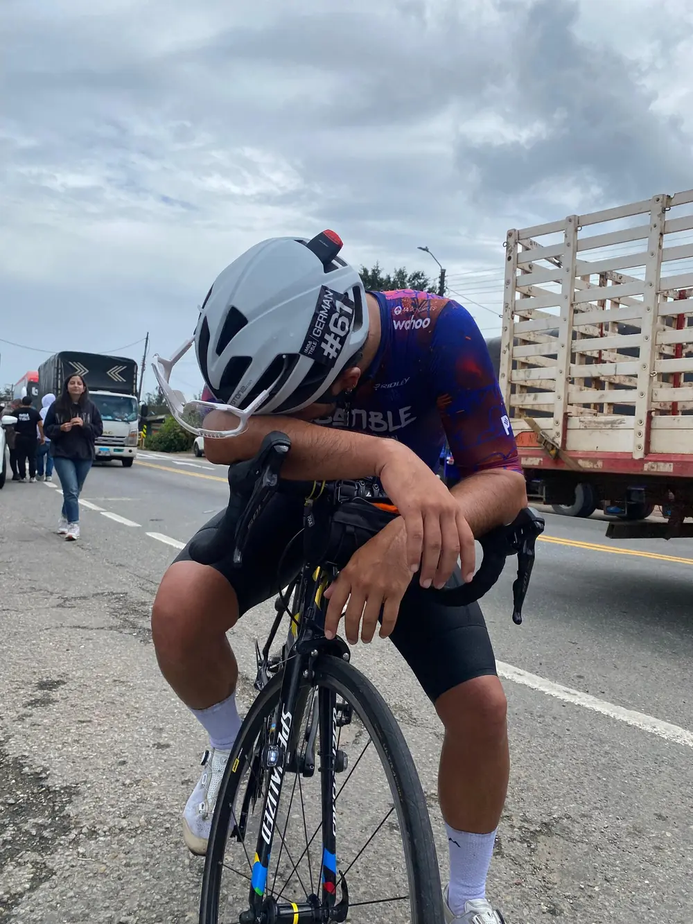 Ciclista exhausto apoyado sobre el manubrio al borde de la carretera